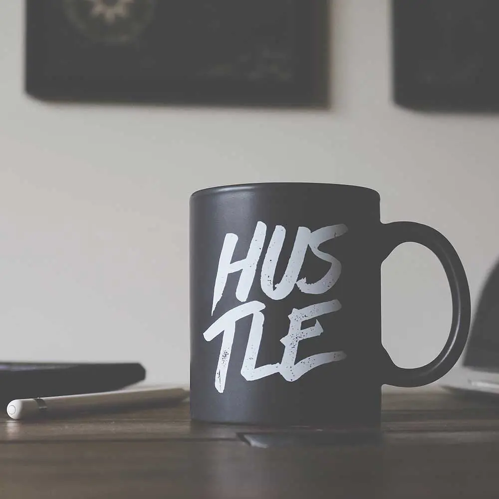 A black coffee mug with the world Hustle on it