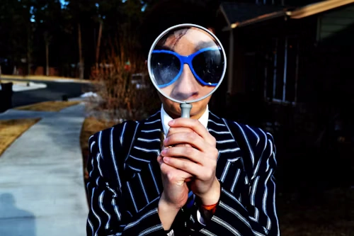 Person using magnifying glass enlarging the appearance of their nose and sunglasses